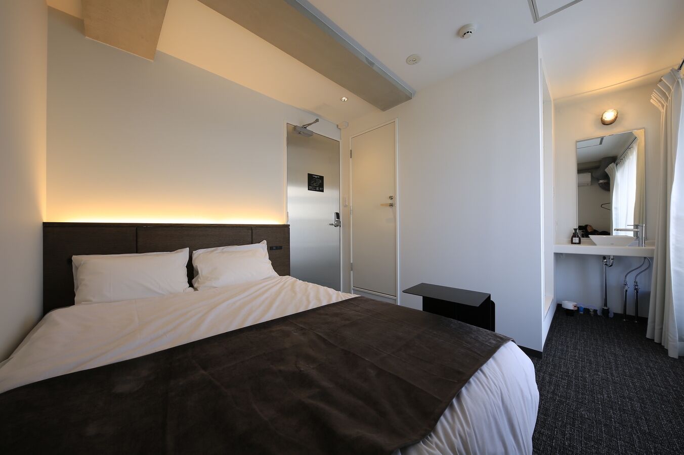 Ein Hotelzimmer mit Bett, Nachttisch und einem Badezimmer mit Waschbecken und Spiegel.