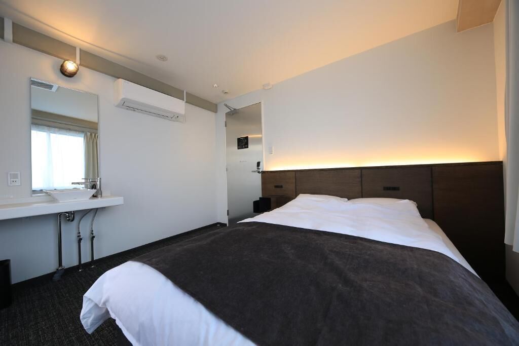 Ein Hotelzimmer mit Bett, Nachttisch, Spiegel, Waschbecken und Klimaanlage.