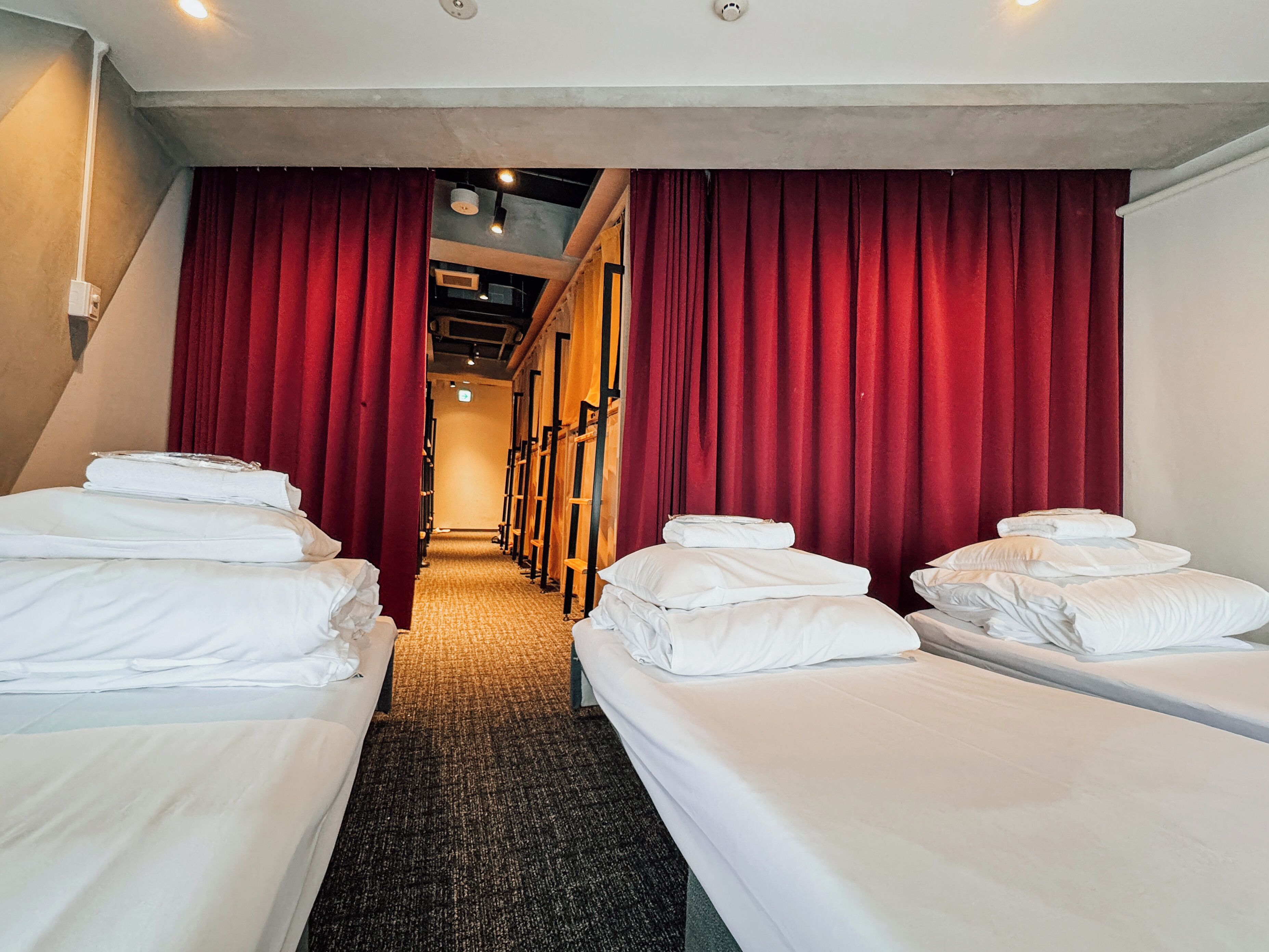 A hotel room with two single beds, red curtains, and a carpeted floor.