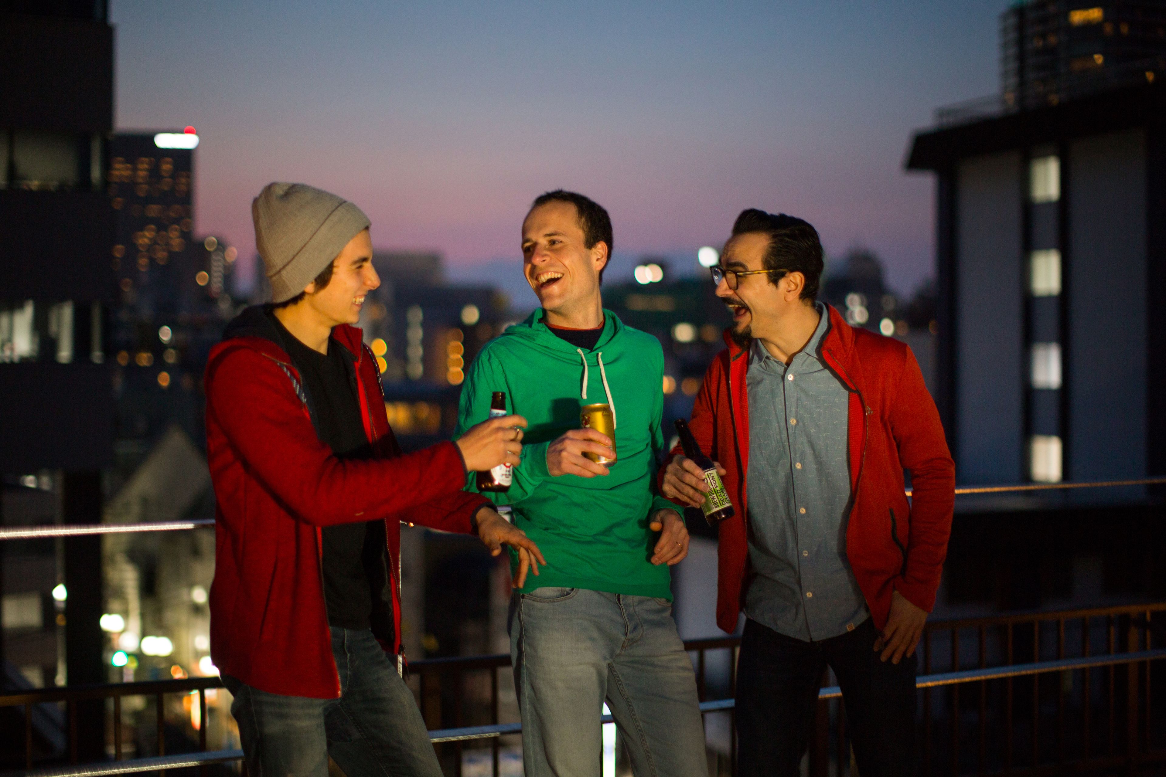 Trois personnes se tiennent sur un balcon, avec une vue sur la ville en arrière-plan.