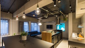 A modern kitchen with a central island, a dining area with a table and chairs, and a living area with a sofa and a TV. - UNPLAN Shinjuku – Hostel (Tokyo)