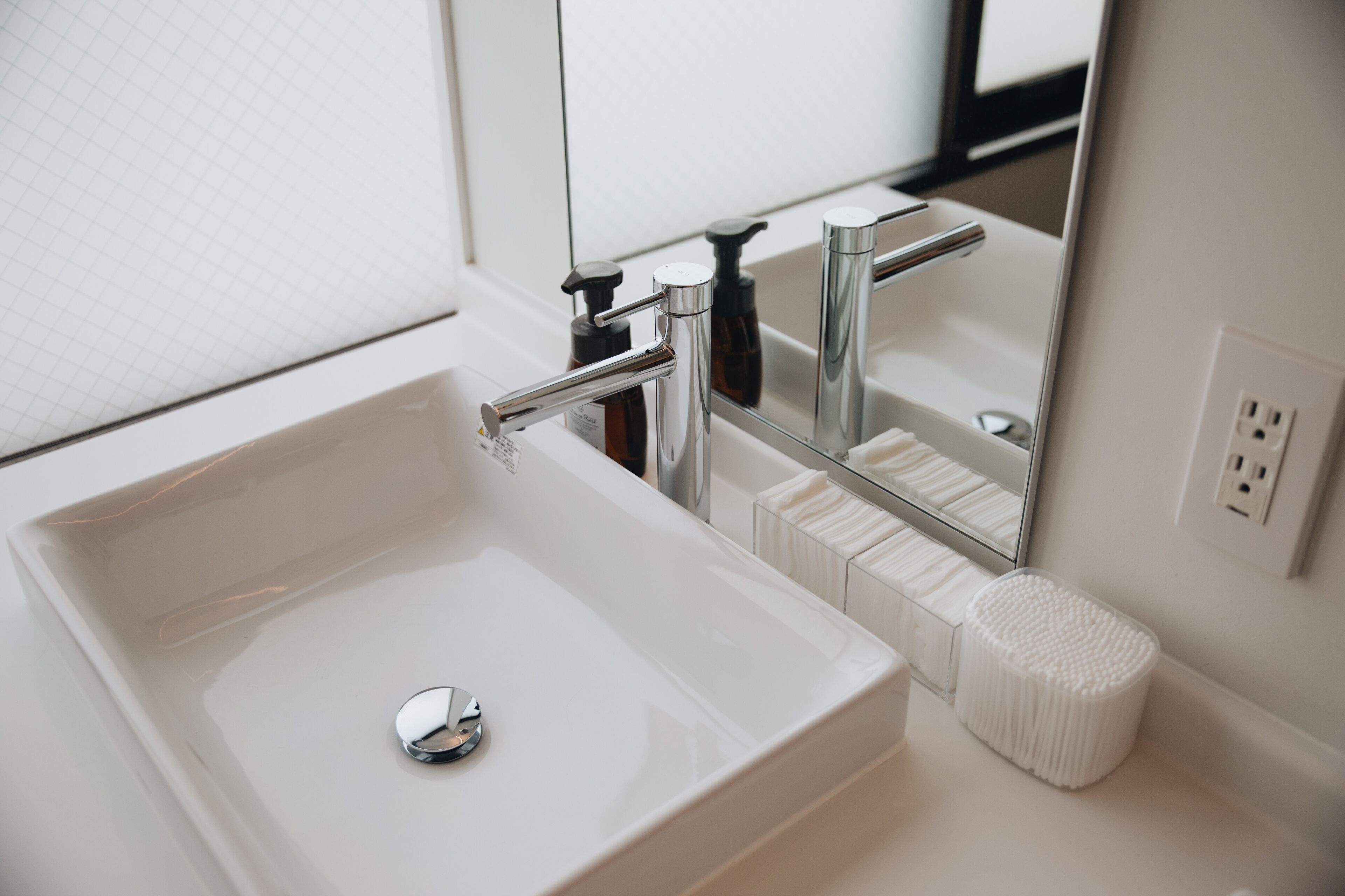 A modern bathroom with a white sink, chrome faucet, and a mirror reflecting the room.