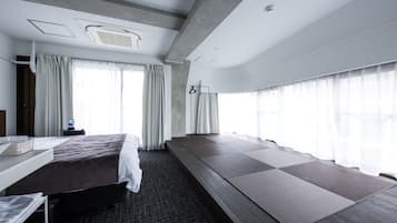 A modern hotel room with a large bed, a desk, and a seating area with mats.