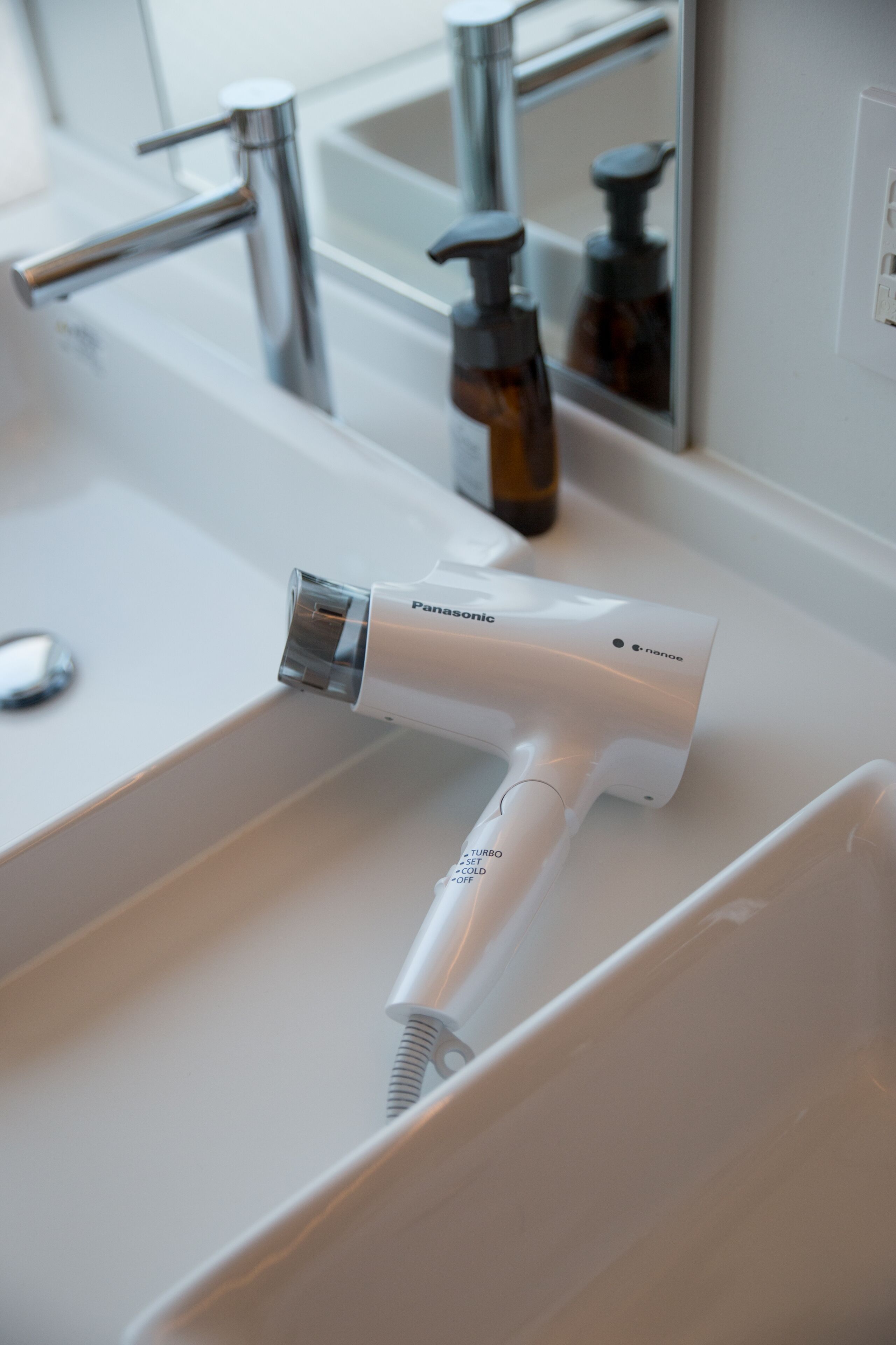 A bathroom sink with a handheld hair dryer and a mirror.