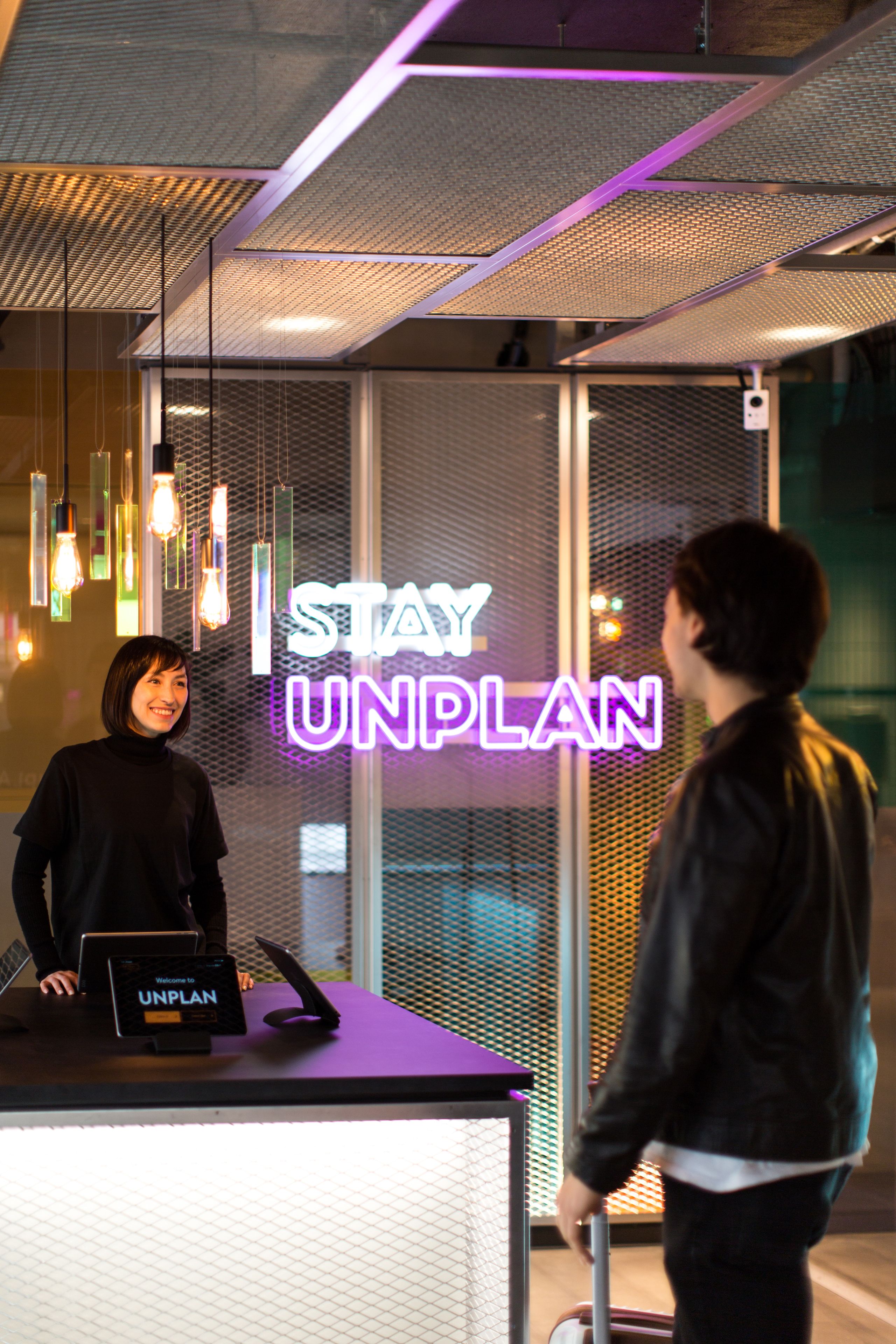 A reception desk with a neon sign that reads "STAY UNPLAN" and a sign that says "Welcome to UNPLAN".