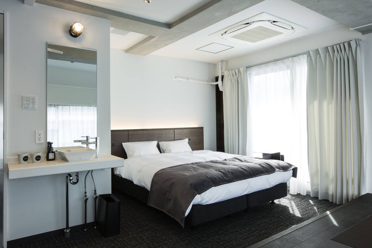 A modern hotel room with a large bed, a built-in sink, and a large window with curtains.