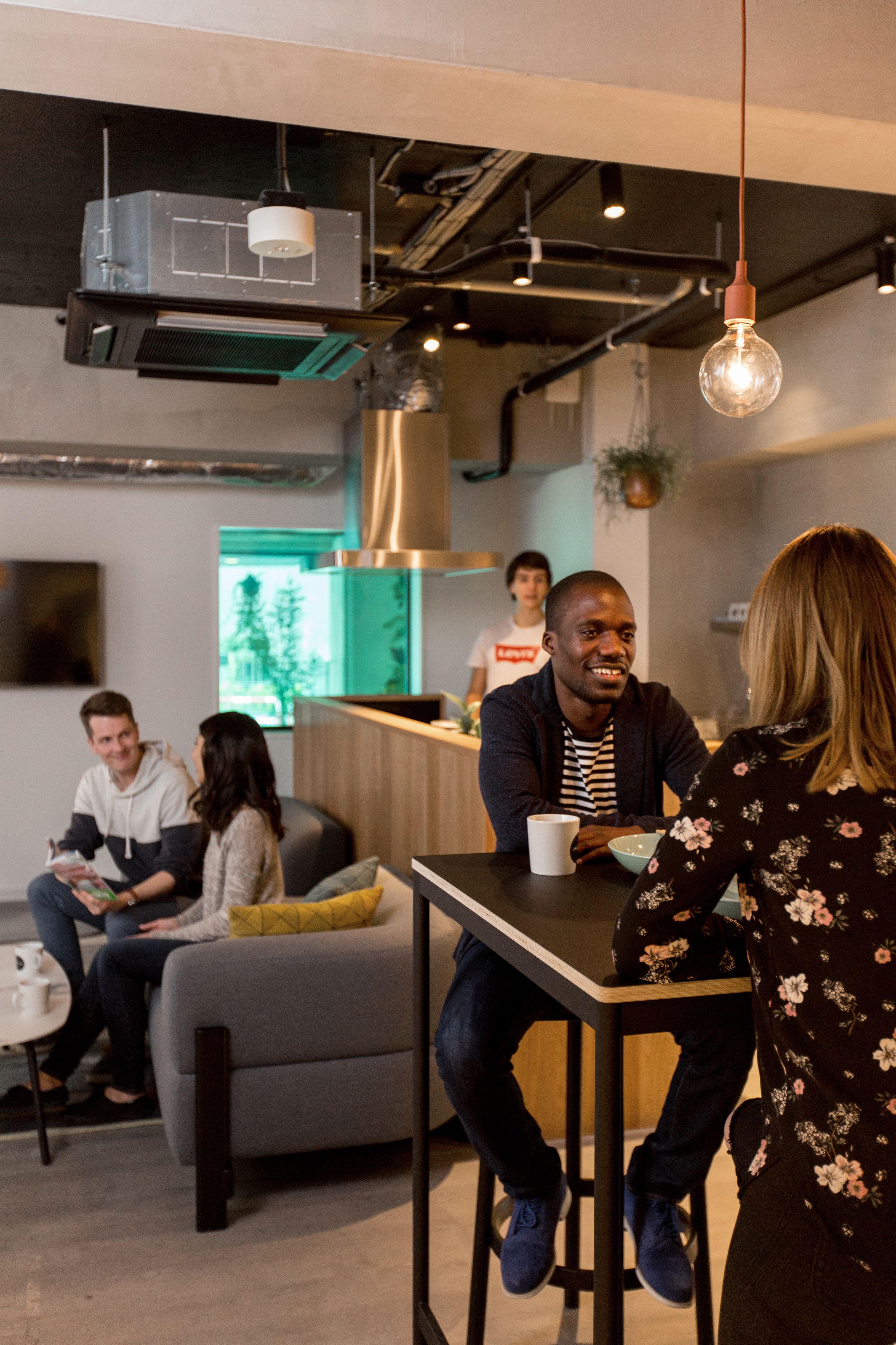 Un intérieur moderne avec un bar, des espaces pour s’asseoir et une cuisine ouverte visible au fond.