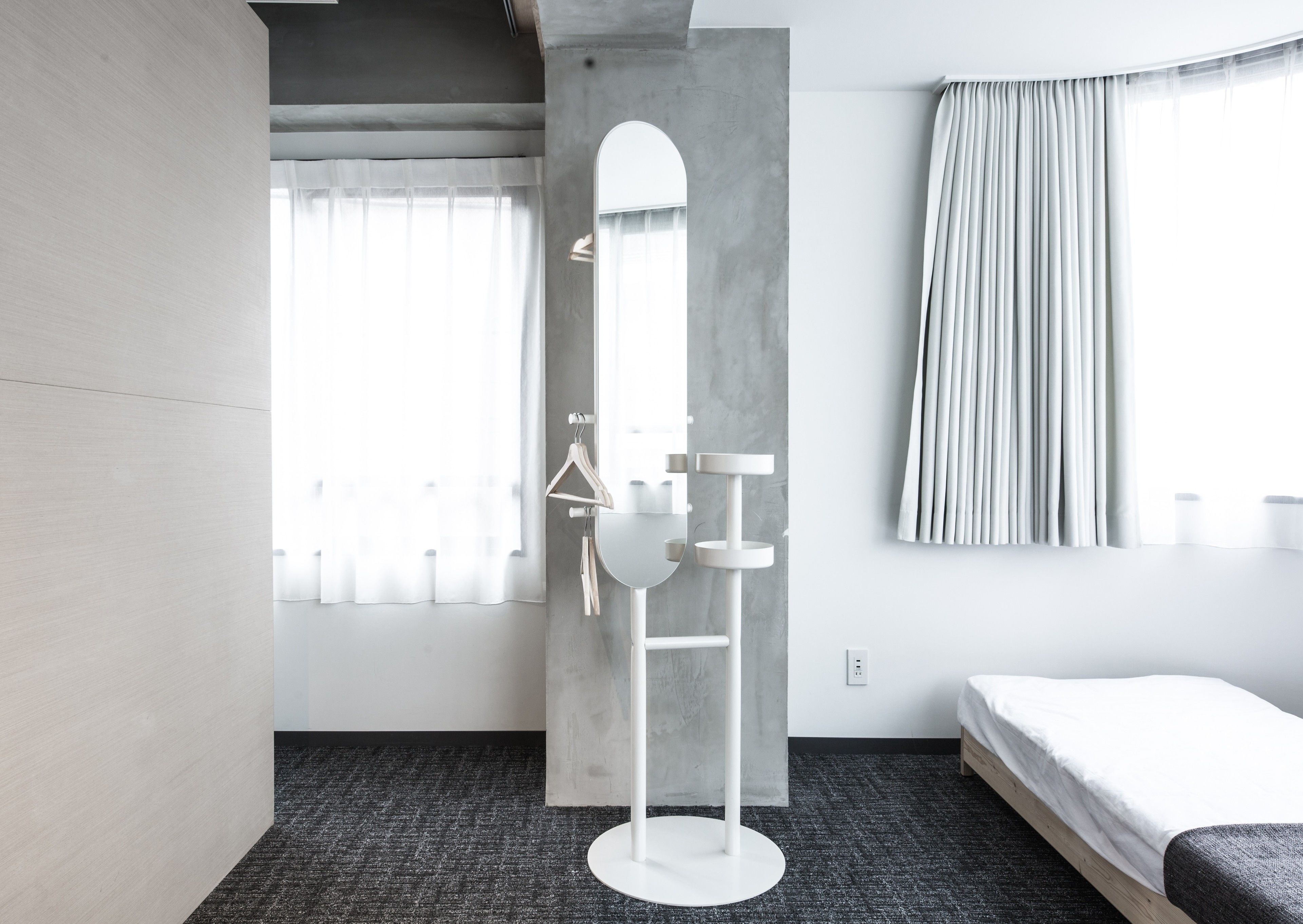 A modern hotel room with a large mirror, a round table, a bed, and a window with curtains.