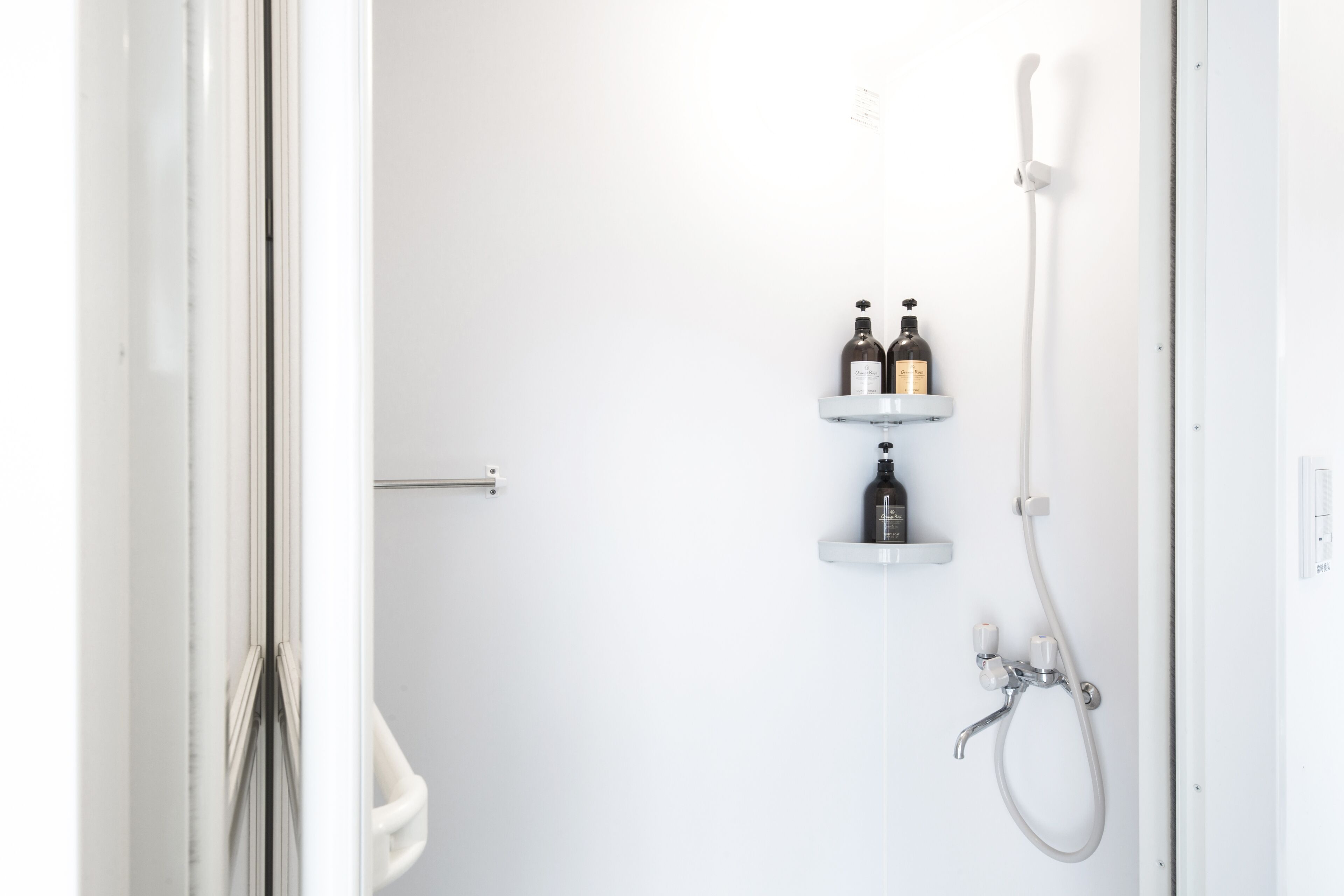 A minimalist bathroom with a white door, a shower with a handheld showerhead, and two bottles on a shelf.