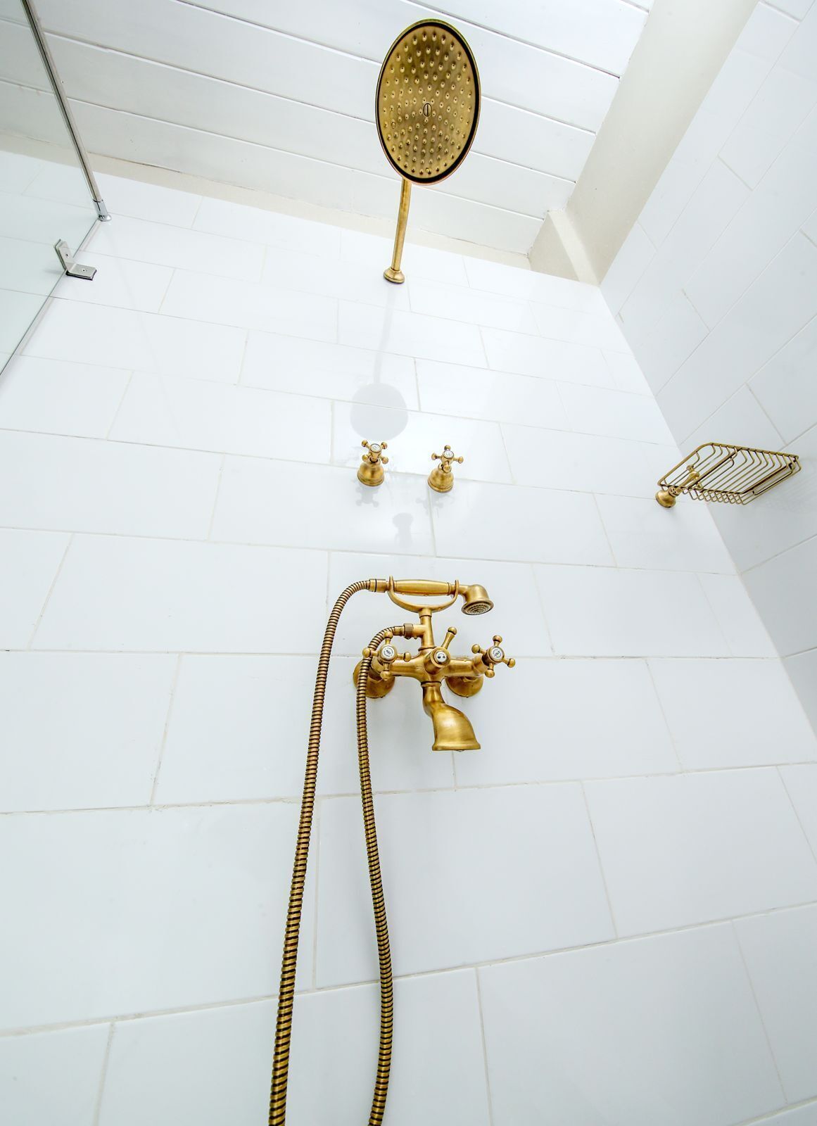Une salle de bain avec un sol carrelé de carreaux blancs, une pomme de douche dorée et un pommeau de douche doré à main.