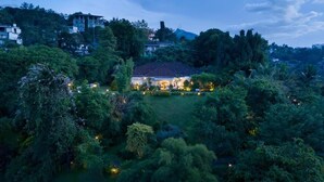 A house surrounded by dense greenery, with a well-lit front yard and multiple windows. - Castle Hill Bungalow by Seven Angels (Kandy)