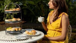 A person seated at a round table with a tiered dessert stand, outdoors with greenery in the background. - Castle Hill Bungalow by Seven Angels (Kandy)