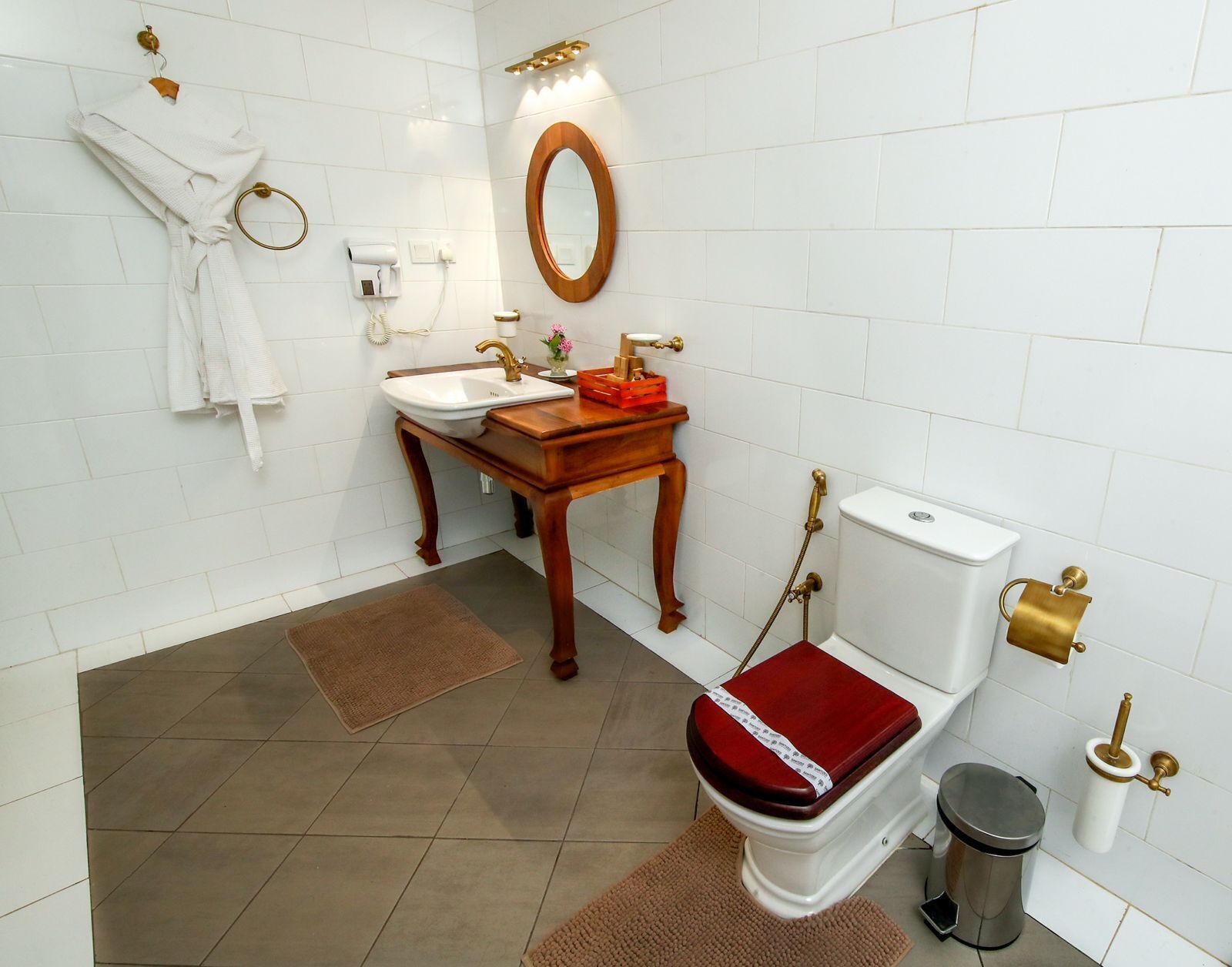 A bathroom with a white sink, wooden vanity, a mirror, a toilet, and a trash can.