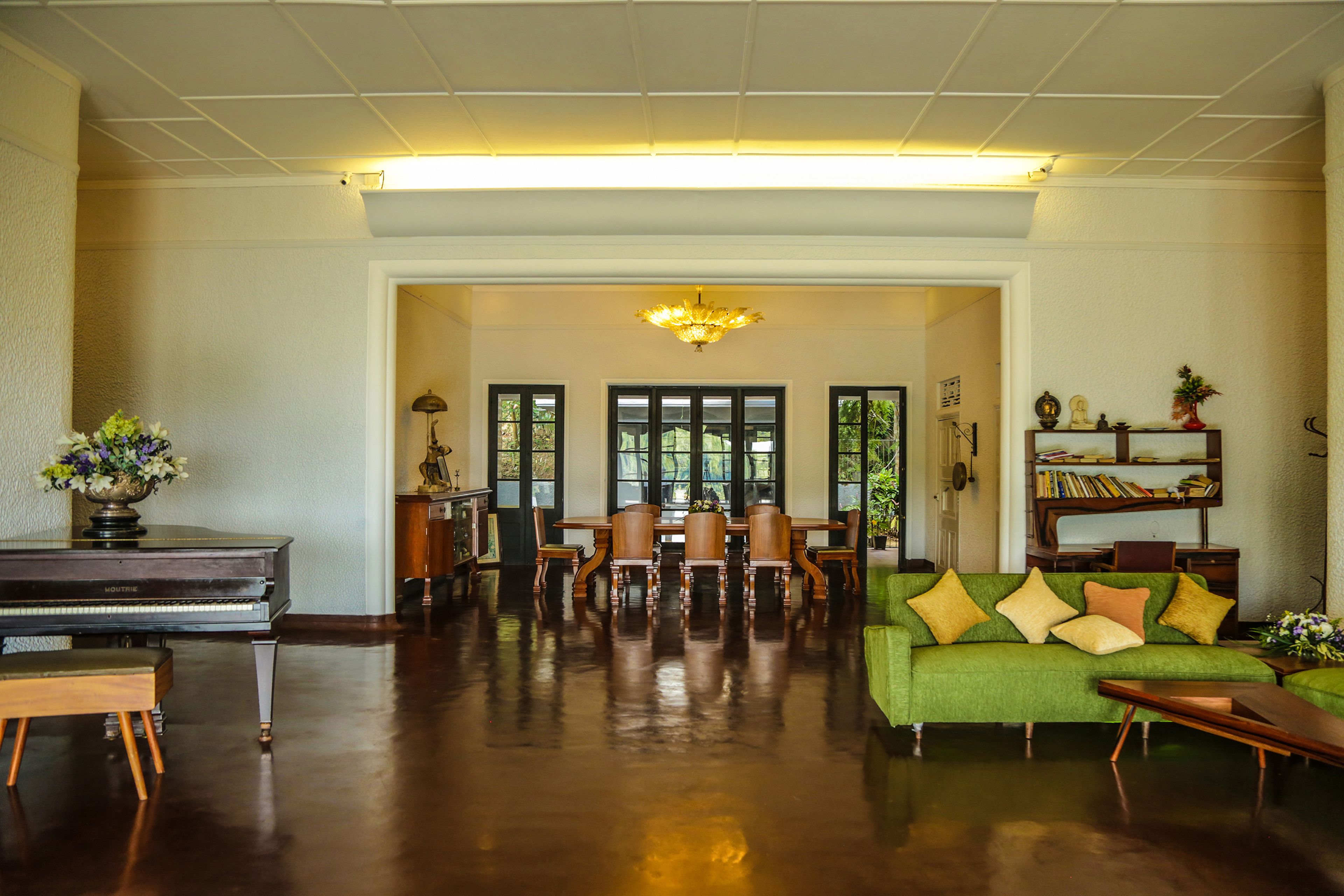 A spacious living room with a grand piano, a green sofa, and a dining area with a wooden table and chairs.