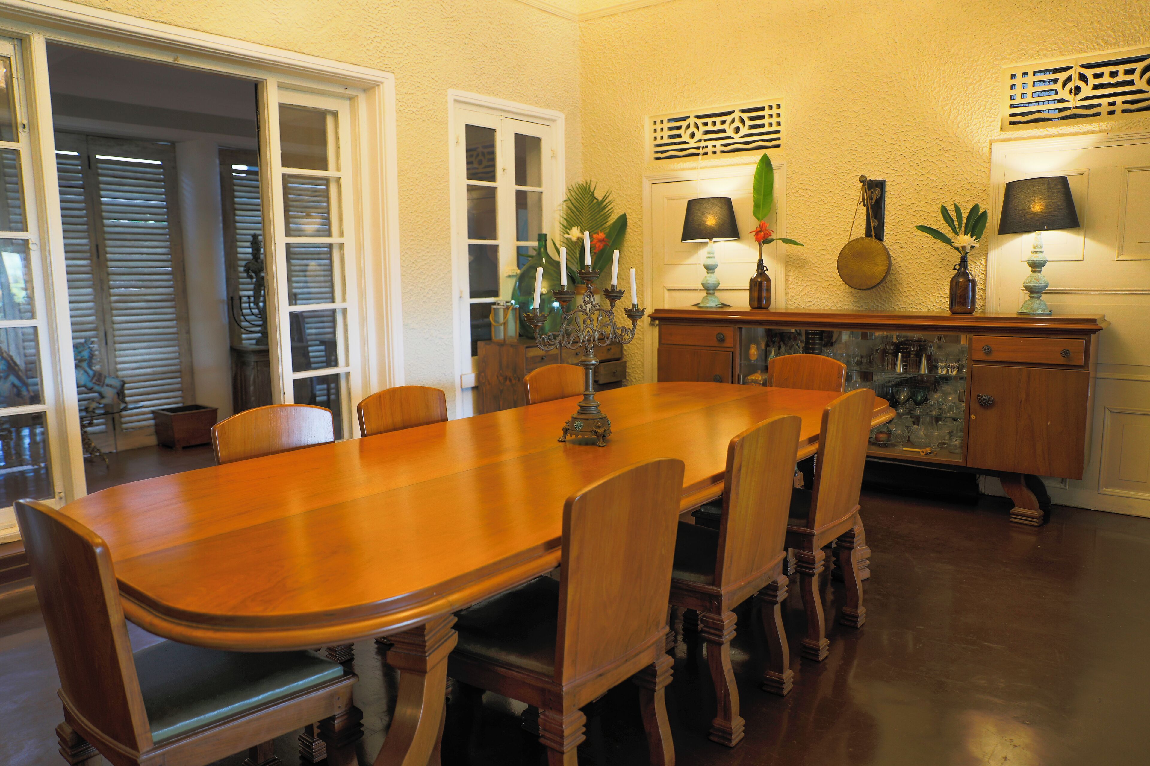 A dining room with a large wooden table, six chairs, a cabinet with decorative items, and a door leading to another room.
