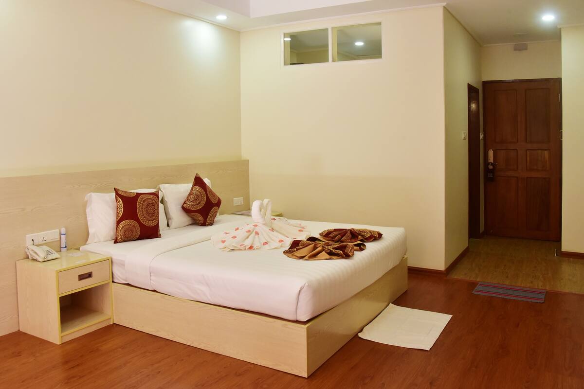 A neatly made bed with a white and pink bedspread, a wooden headboard, and a bedside table with a phone and a bottle.
