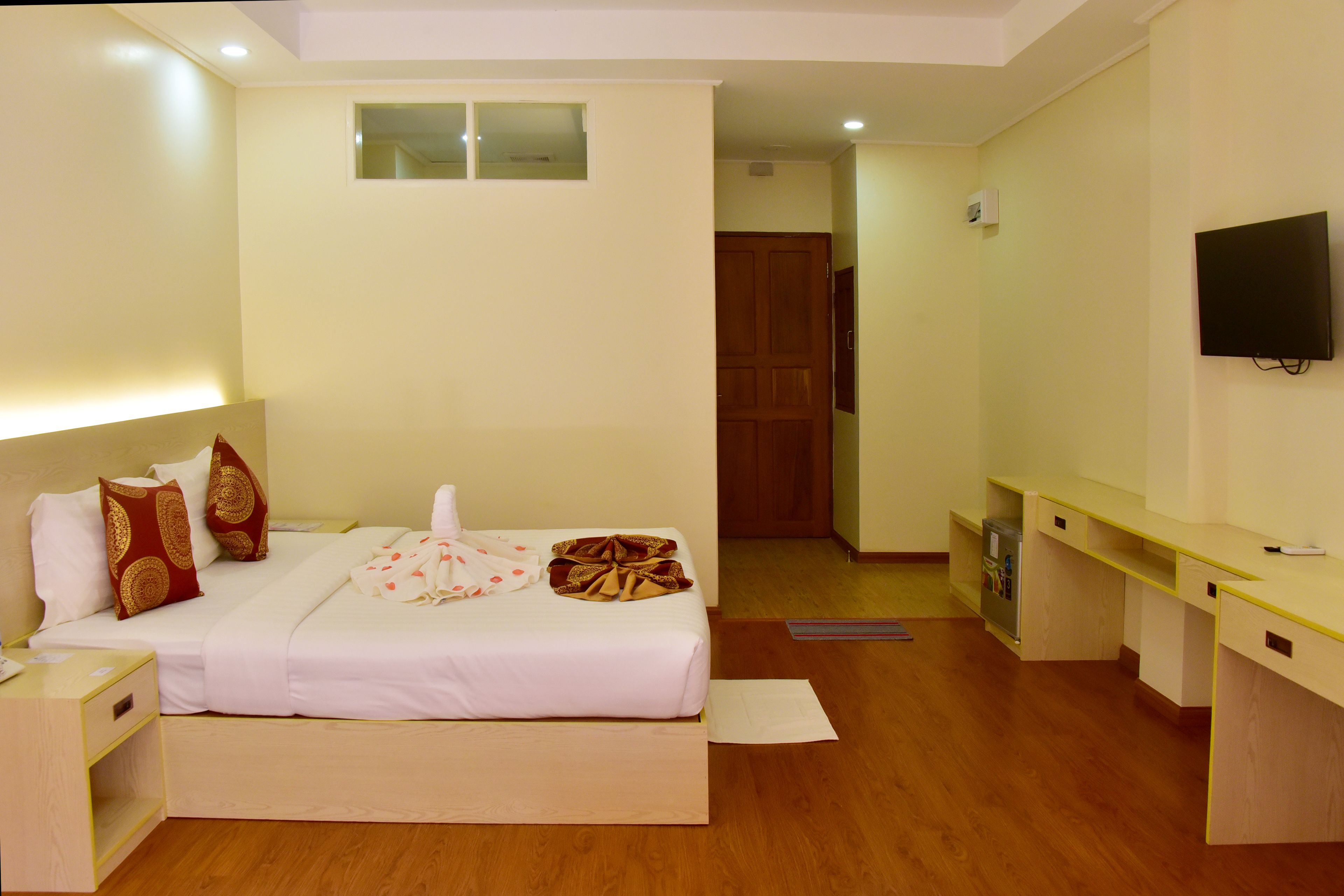 Habitación de hotel con cama, mesita de noche, televisión y un pequeño escritorio.