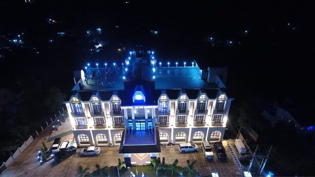A large, multi-story building with a central courtyard, surrounded by parked cars and a few trees. - Hotel Mya Yar Pin (Kalaw)