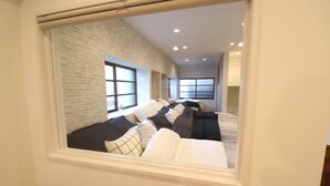 Una habitación con pared de ladrillo, una ventana grande y una cama con muchas almohadas.