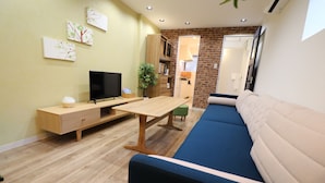 Una sala moderna con un mueble bajo para el televisor de madera, un televisor de pantalla plana, una mesa de comedor, un sofá azul y una pared de ladrillo decorativa.
