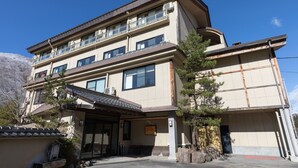 A multi-story hotel with a flat roof, large windows, and a covered entrance area with a small garden. - Tabist Kazeyuki (Takayama)