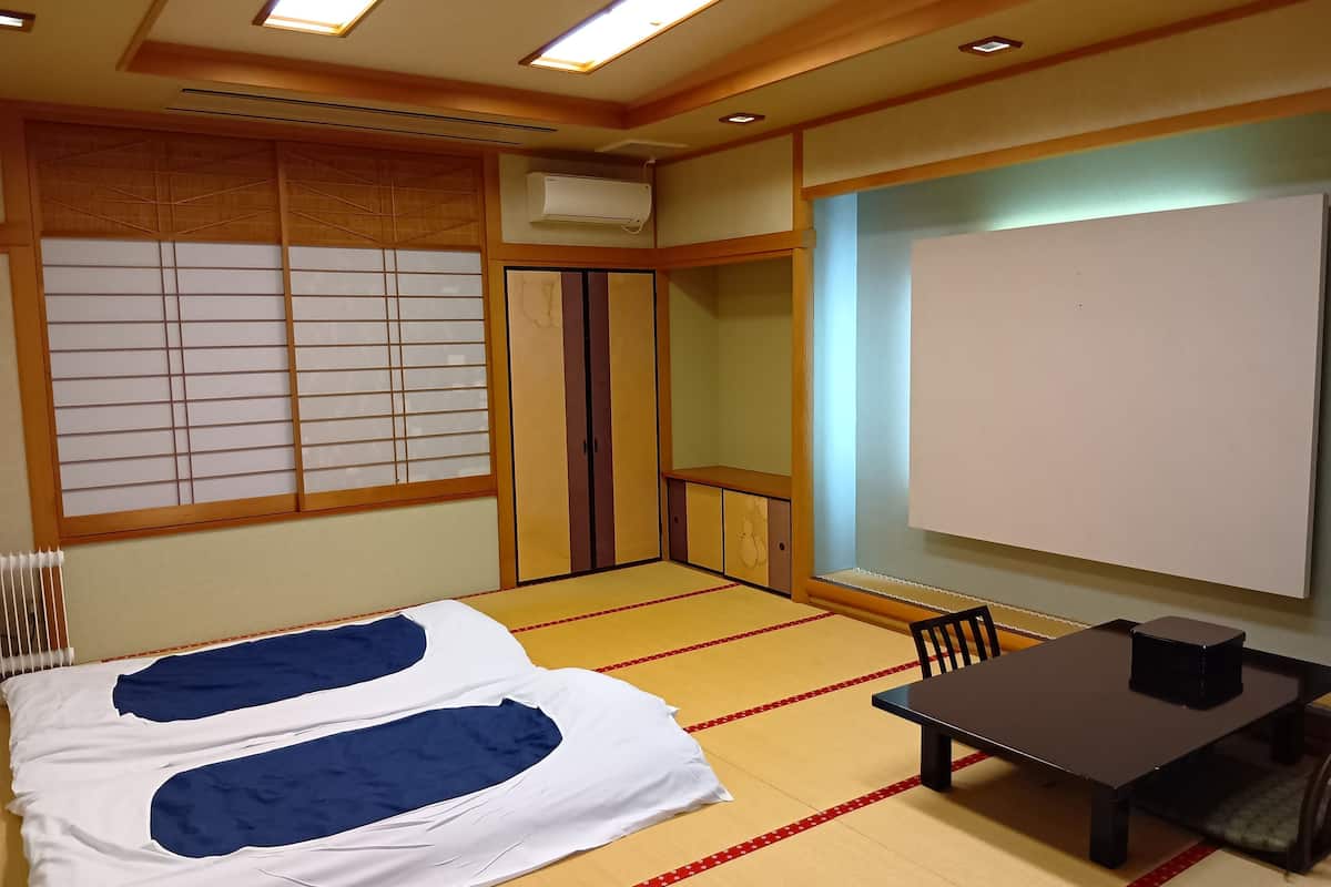 A room with tatami flooring, a bed with blue and white bedding, a small table with a black object, and a whiteboard on the wall.