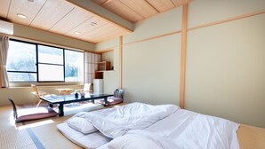 A traditional Japanese-style room with tatami flooring, a futon bed, a low table with chairs, and a large window providing a view of the outdoors. - Tabist Kazeyuki (Takayama)