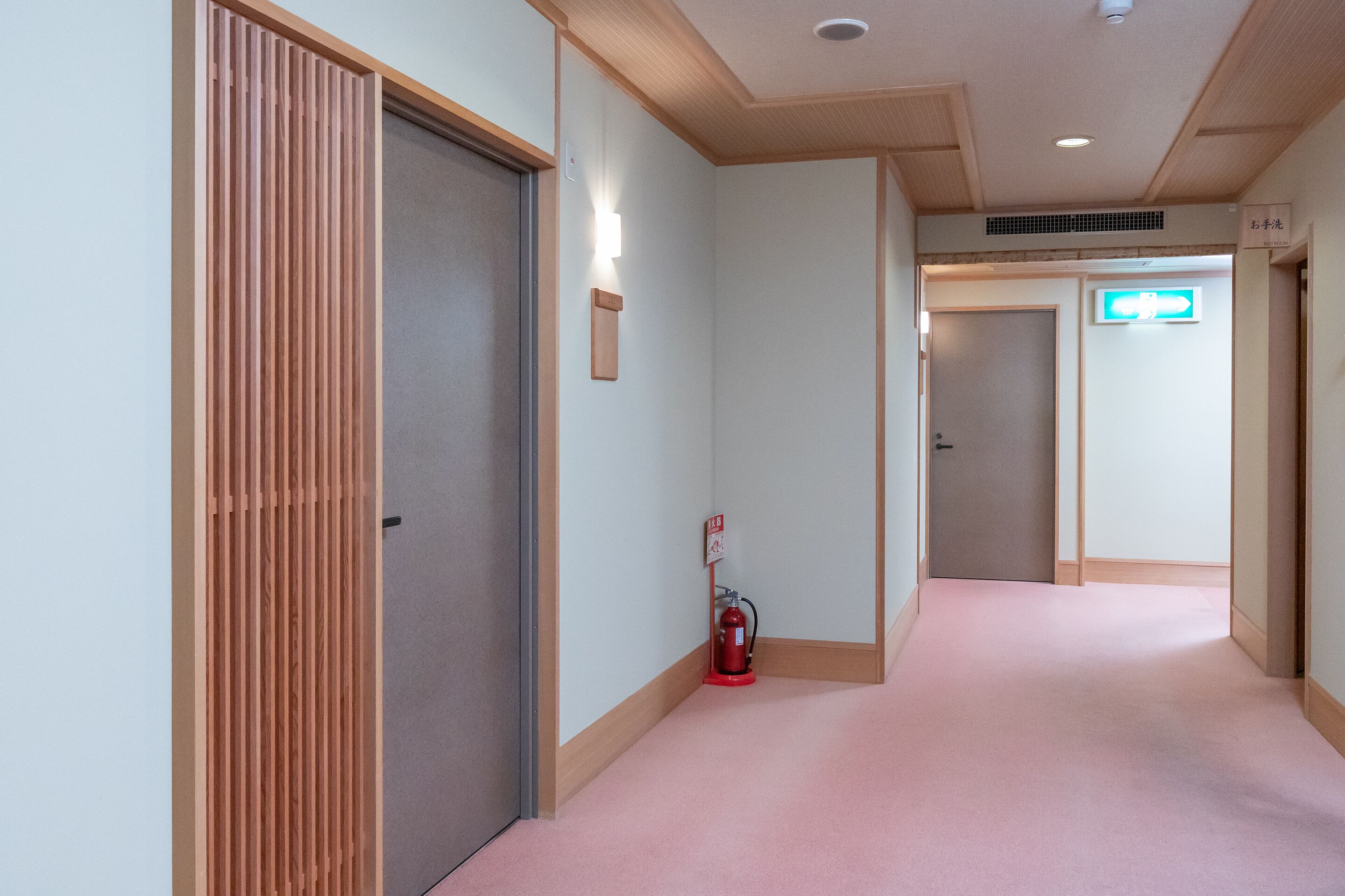 A hallway with a fire extinguisher, a door with a sign, and a neon exit sign.