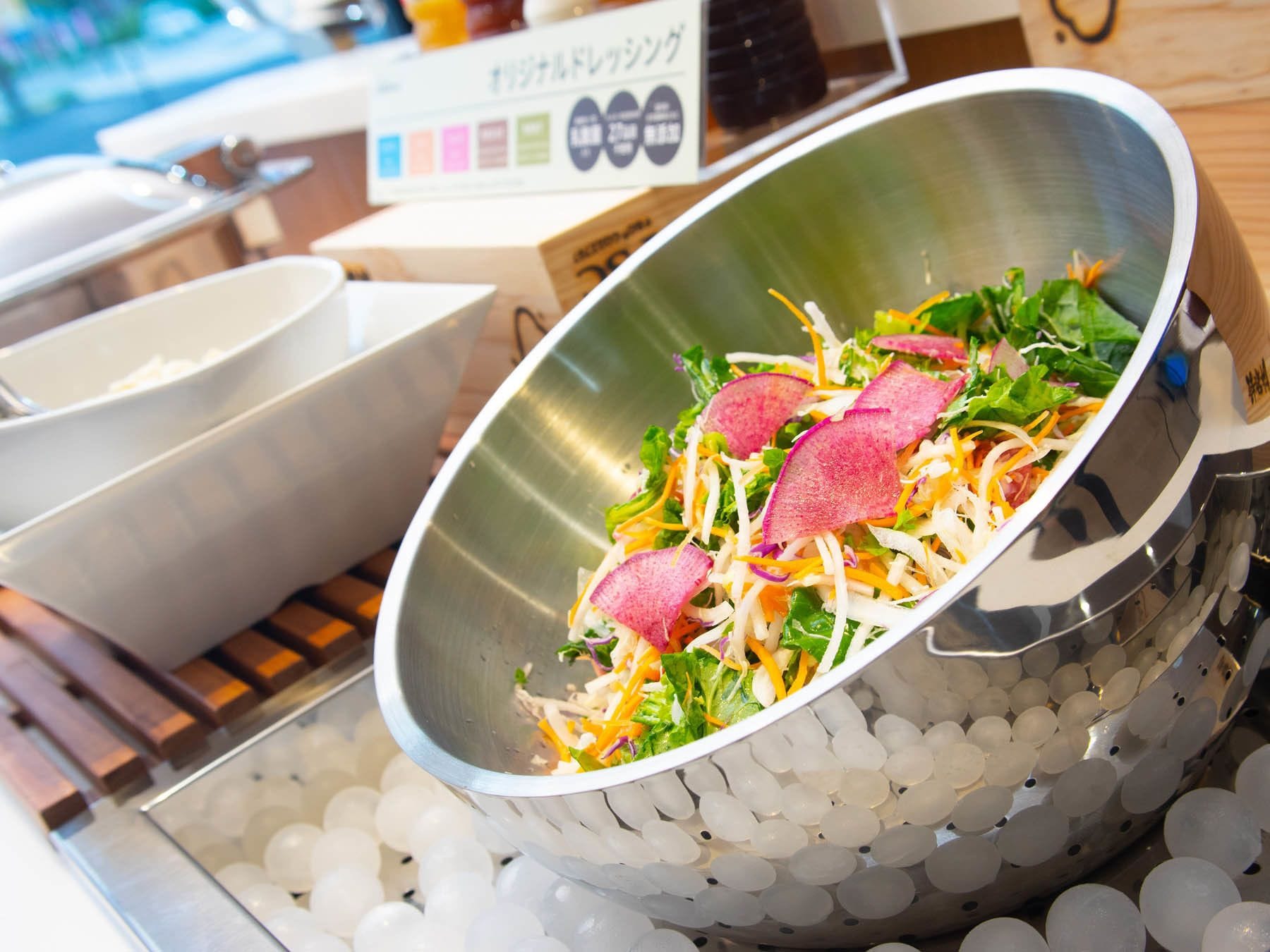 A salad bowl on a tray with ice balls underneath.