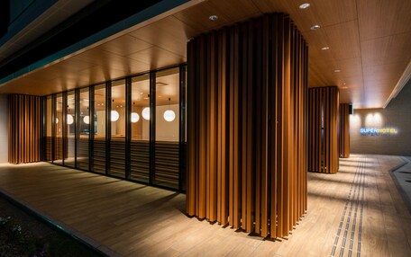 A modern hotel entrance with a wooden facade, glass doors, and a sign reading "Super Hotel".