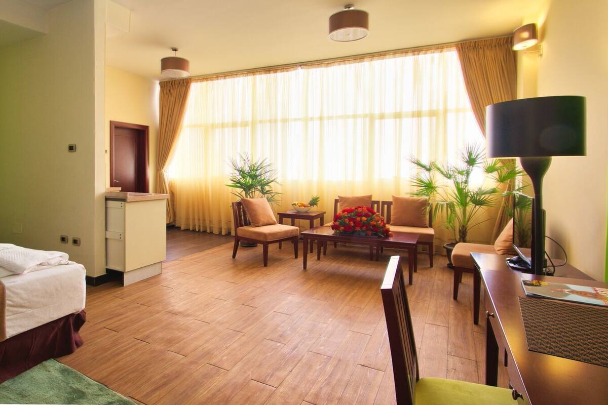 A hotel room with a bed, a desk, a chair, a sofa, a coffee table, and a TV.