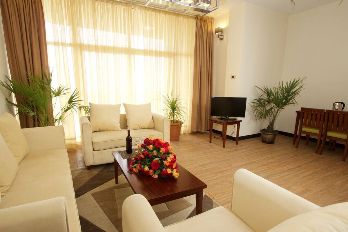 A living room with a sofa, a coffee table with a flower arrangement, a TV, and a dining area with chairs.