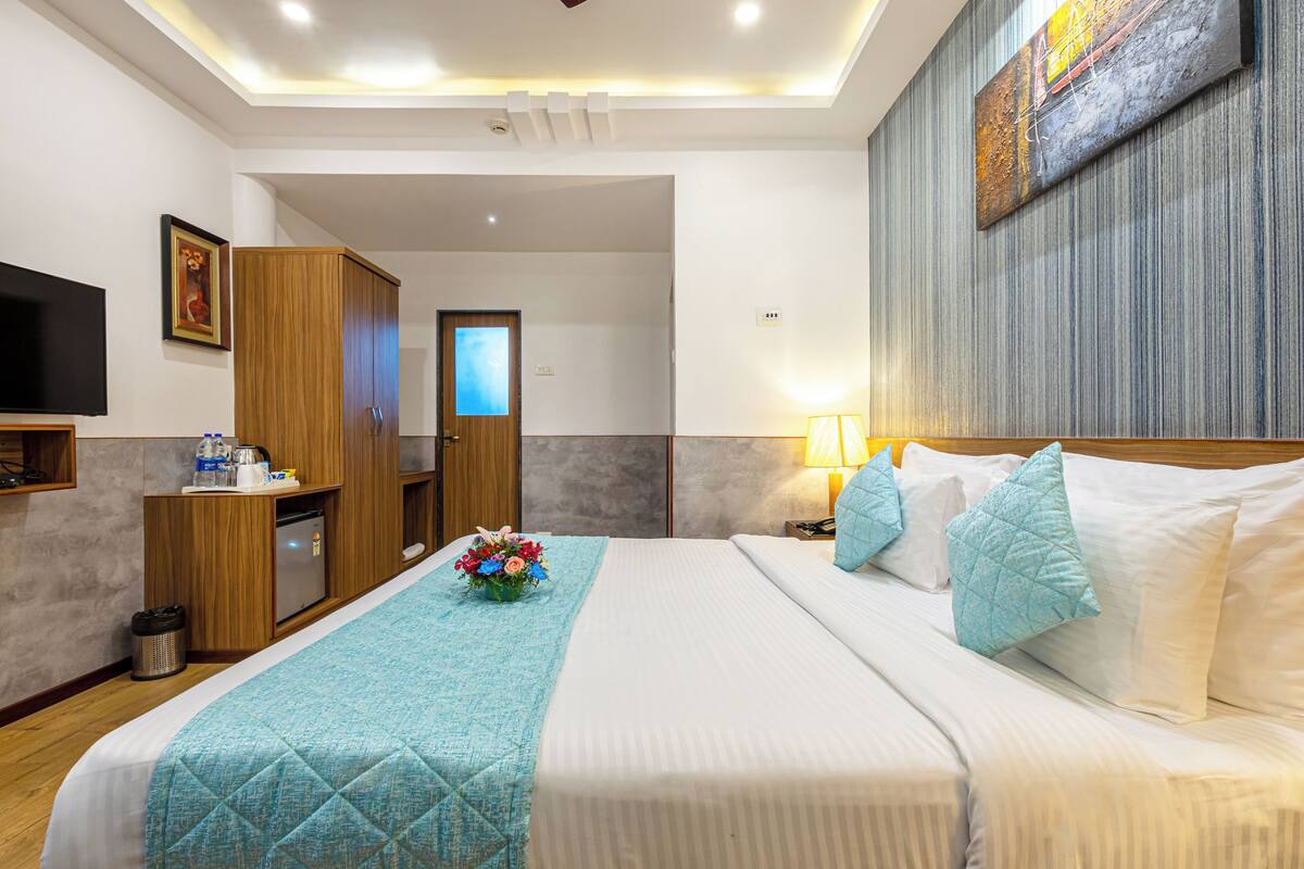 A hotel room with a bed, a desk, a TV, and a painting on the wall.