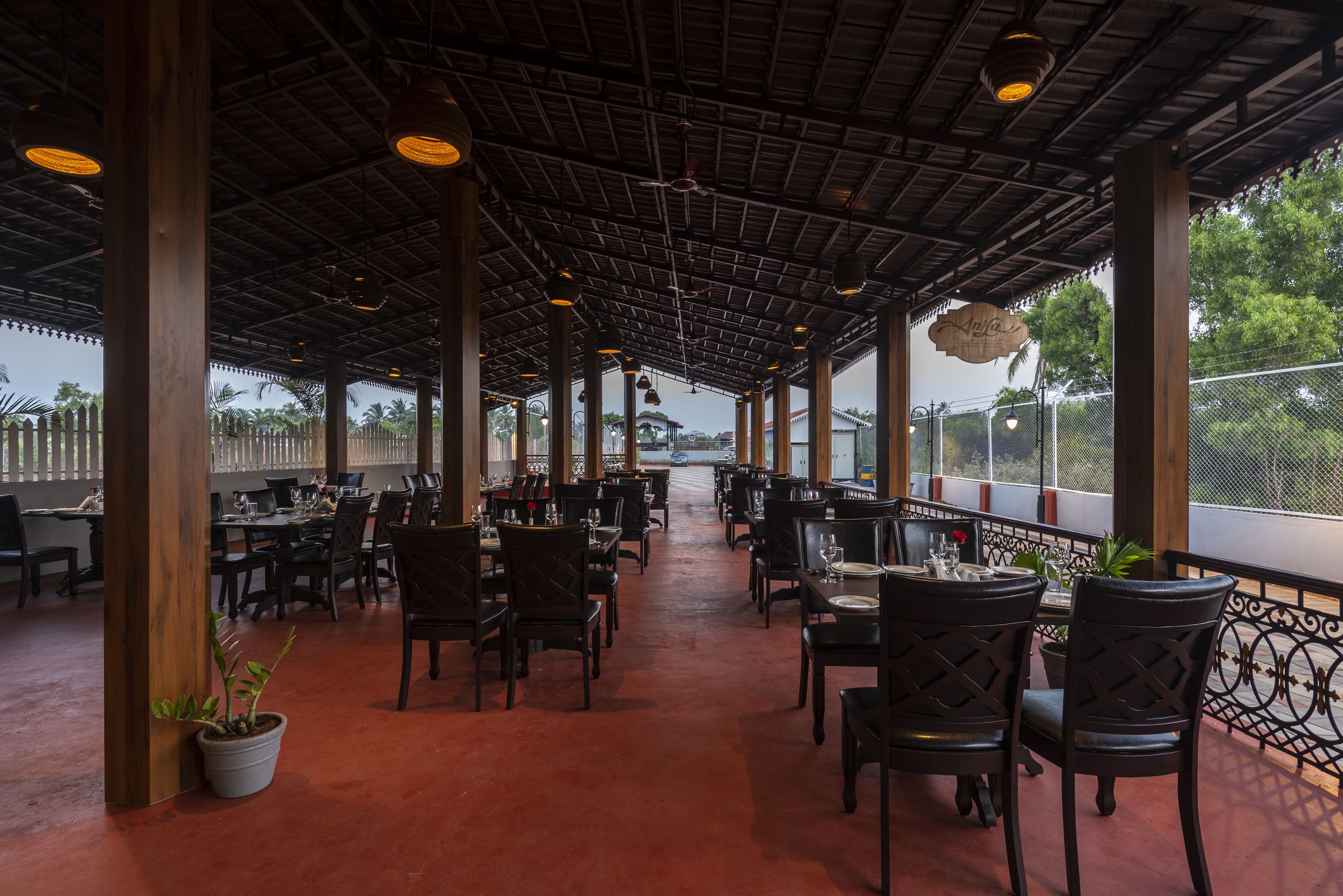 An indoor dining area with tables and chairs, a high ceiling with exposed beams, and a view of the outdoors.
