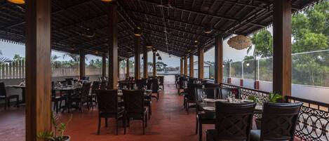 An indoor dining area with tables and chairs, a high ceiling with exposed beams, and a view of the outdoors.