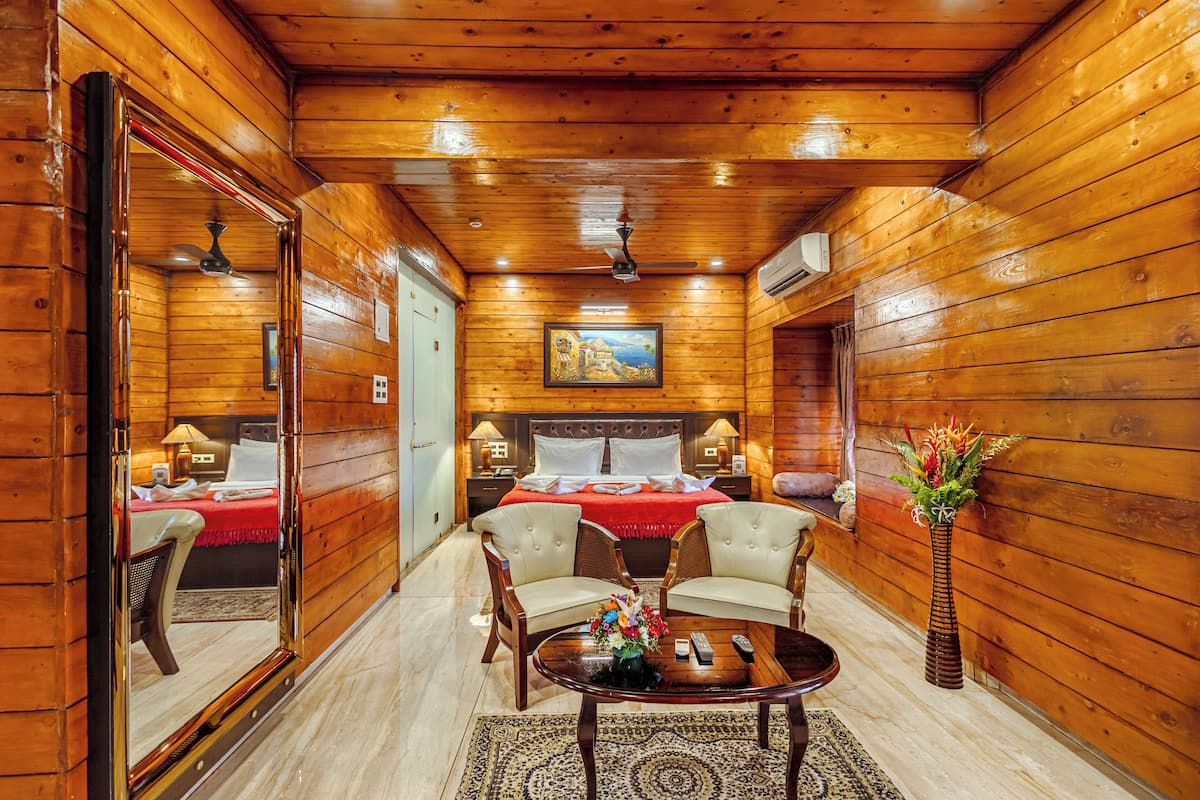 A wooden-paneled room with a bed, two armchairs, a coffee table, and a vase of flowers.