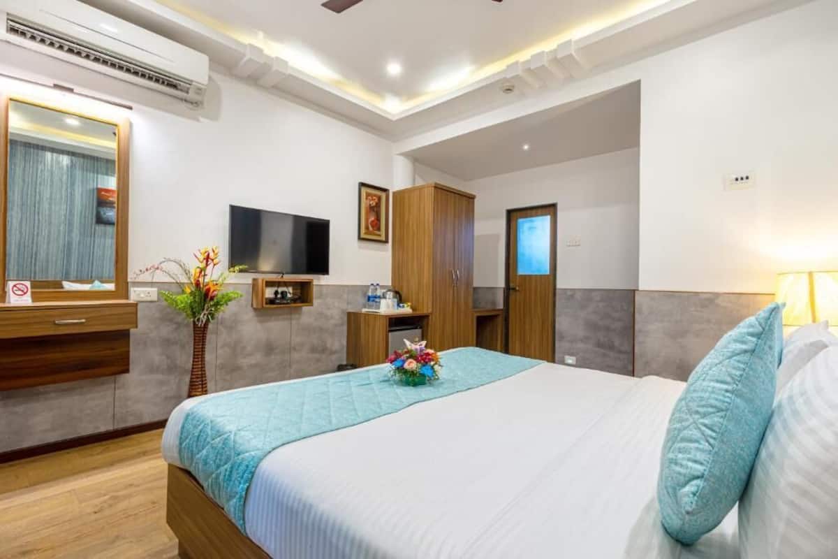 A hotel room with a bed, a television, a wardrobe, a desk, and a mirror.