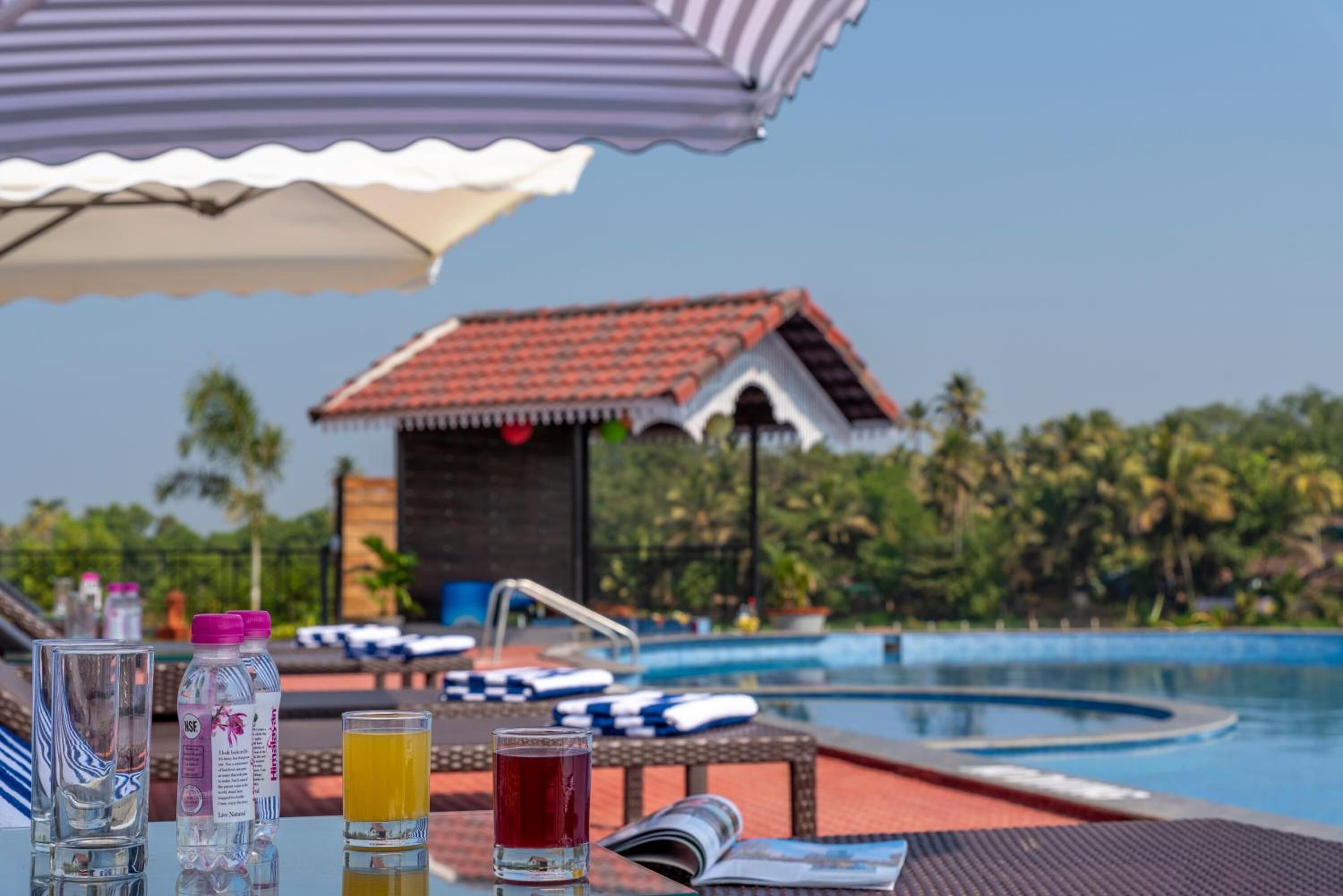 A poolside table with drinks and a magazine, lounge chairs, and a pool.
