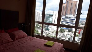 Un cuarto de hotel con una cama grande, vistas de la ciudad a través de una ventana y el horizonte urbano al fondo.