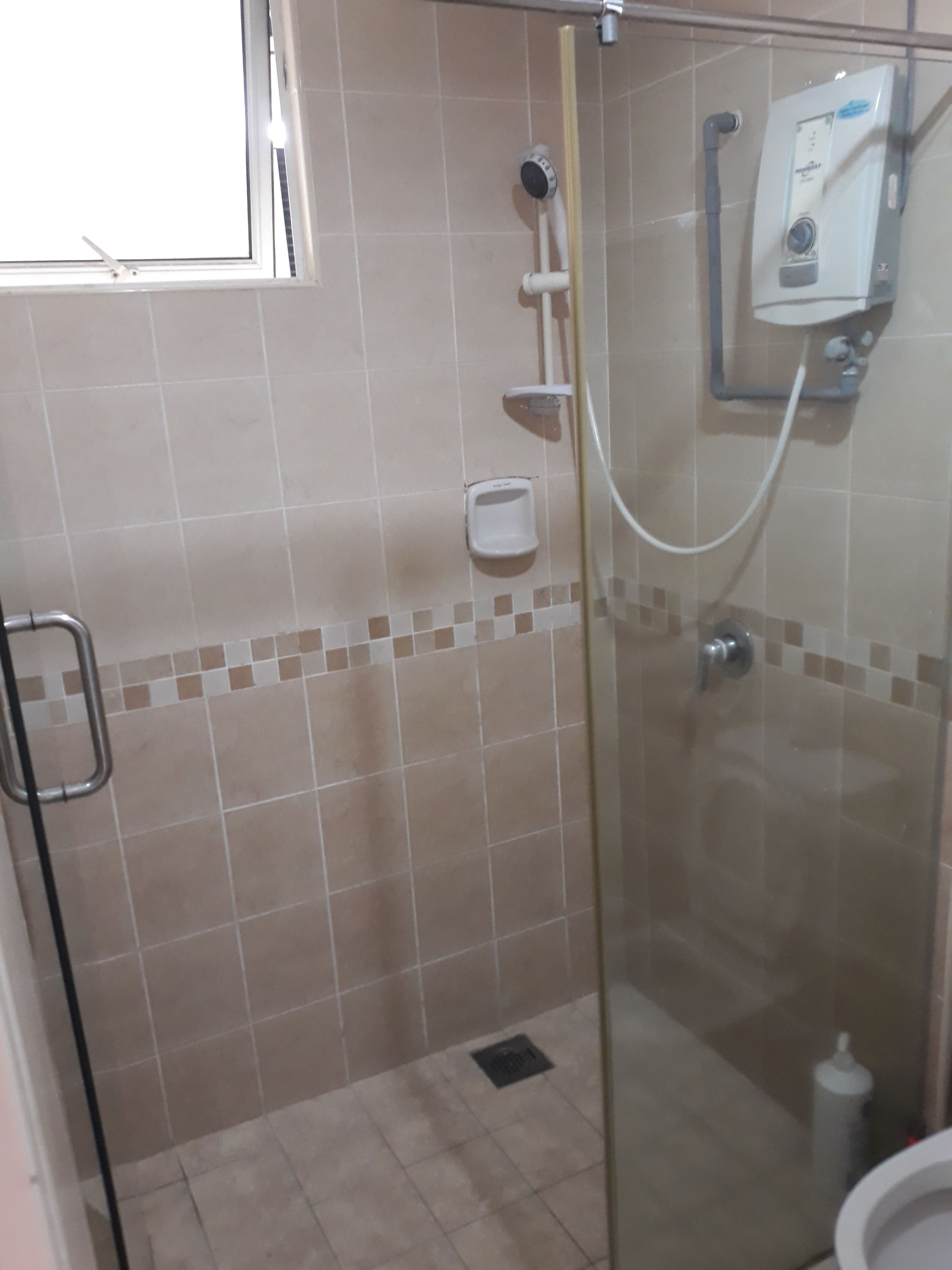 Un área de ducha con cerramiento de vidrio, con ducha de mano, panel de control en la pared y dispensador de jabón de mano.