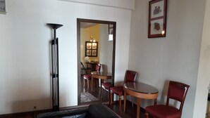 Una sala de estar con un sofá de cuero negro, una mesa de comedor con cuatro sillas y un espejo que refleja un comedor con una araña.