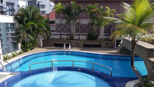 Una piscina circular con borde de azulejos, rodeada de palmeras y un edificio con techo de tejas rojas al fondo.