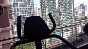 Vista desde un balcón con equipo de ejercicio, con vistas a edificios altos y una piscina.