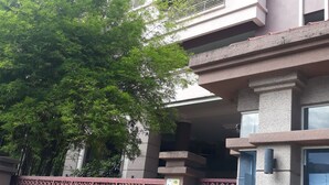 Un edificio de varios pisos con balcones, un acceso con puerta de rejas y un árbol en la entrada.