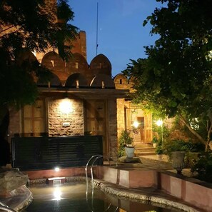 Un edificio tradicional con ventanas de arco y fachada de piedra, una pequeña piscina y plantas en macetas.