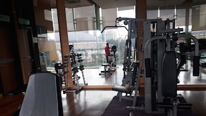 Un gimnasio con equipo de ejercicio, un espejo y vistas a un paisaje urbano.