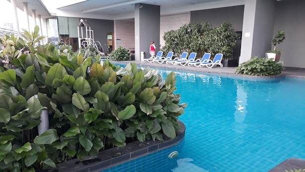 Una piscina interior con suelo de baldosas azules, rodeada de exuberante vegetación y sillones reclinables azules.