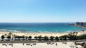 Vista costera con playa, paseo marítimo y una carretera con coches estacionados.