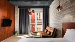 Una habitación de hotel moderna con una cama grande, un sofá de cuero, una pequeña mesa redonda y un televisor montado en la pared.