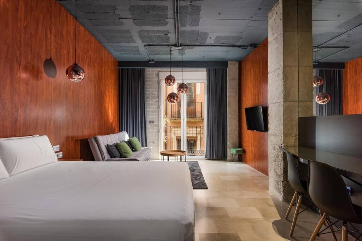Una habitación de hotel moderna con una cama grande, un sofá, un televisor y un balcón con vistas.